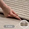 A close-up of a hand touching a rug, with a measurement indicator. Voir les images du produit