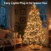 A decorated Christmas tree with warm white lights in a cozy living room setting, with a sofa and window in the background. Voir les images du produit