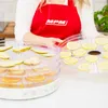 A person in a red apron is holding a tray of sliced lemons next to a food dehydrator filled with sliced pears and oranges. Náhľad obrázku produktu