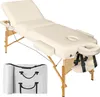 A cream-colored, three-zone massage table with wooden legs and a headrest, shown in a studio setting against a white background. A folded carrying case is visible in the foreground. Náhled obrázku produktu