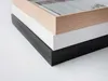 A close-up view of three stacked picture frames with different colored borders: wood, white, and black. Anteprima dell’immagine prodotto