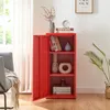 A red metal cabinet with its door open, displaying items on shelves, placed in a room with a chair and a plant. Voir les images du produit
