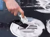 A hand is using a glass scraper to clean a black glass stovetop. Náhľad obrázku produktu
