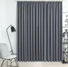 A grey curtain is shown hanging in a room, with a floor lamp and a chair to the left, and a shelf with decorative items to the right. Produktbild-Vorschau