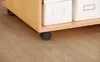 A close-up view of the bottom section of a light wood desk with two white storage boxes on top and black casters on the bottom. Produktbild-Vorschau