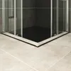 A close-up view of a modern shower cabin corner with a black shower tray and tiled walls, set against a tiled floor. Produktbild-Vorschau