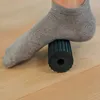 A person's foot wearing a gray sock is resting on a black foam roller on a wooden floor. Produktbild-Vorschau