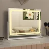 A lighted makeup mirror on a vanity table, with artwork and makeup brushes in the background. Produktbild-Vorschau