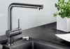 A modern kitchen faucet with a pull-out spout is shown on a dark countertop next to a sink. A potted plant is visible in the background. Anteprima dell’immagine prodotto