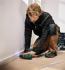 A man is kneeling and using a cordless drill to install baseboards in a room. Produktbild-Vorschau