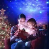 A mother and daughter are opening a gift in front of a Christmas tree, with a starry night sky projected onto the ceiling. Náhled obrázku produktu