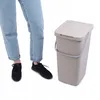 A person's legs wearing jeans and black sneakers stand next to a brown plastic trash can with a lid and handle. Podgląd zdjęcia produktu
