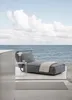 A modern outdoor lounge chair with a blanket is placed on a deck overlooking the ocean. Podgląd zdjęcia produktu