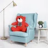 A red teddy bear sits on a light blue armchair next to a small side table with a plant, alarm clock, and vase. Podgląd zdjęcia produktu