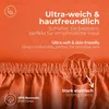 Close-up of an orange fabric, likely a bedsheet, with text overlays highlighting product features. Produktbild-Vorschau