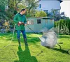 A man is pressure washing a wheelbarrow in a backyard with a shed and a house in the background. Produktbild-Vorschau