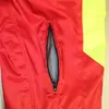 A close-up view of a red garment with a yellow panel and a zippered mesh pocket. Produktbild-Vorschau