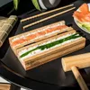 A sushi-making kit with rice, salmon, and chives laid out on a black tray, with chopsticks and a bamboo mallet nearby. Náhľad obrázku produktu