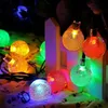 Mehrfarbige LED-Bubble-Lichterkette, hell leuchtend, über einen weißen Lattenzaun und gemusterten Stoff drapiert Produktbild-Vorschau