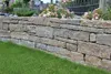 A stone wall with grass in front and flowers behind. Produktbild-Vorschau