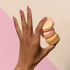 A hand with manicured nails holding macarons against a split-color background. Anteprima dell’immagine prodotto