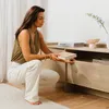A woman is crouching next to a wooden TV cabinet, holding a book. Produktbild-Vorschau