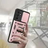 A hand holding a rose gold phone case with a ring holder and camera cover, with a blurred indoor background. Produktbild-Vorschau