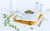 A white coffee service set is arranged on a white table with a yellow napkin and some greenery. Produktbild-Vorschau