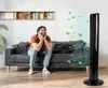 A man sitting on a sofa in a living room, enjoying the breeze from a black tower fan. Anteprima dell’immagine prodotto