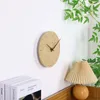 A minimalist wall clock with a stone-like texture is mounted on a white wall, next to a stack of books and a pleated table lamp. Produktbild-Vorschau