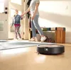 A mother and daughter are walking into a home, with a robot vacuum cleaner on the floor. Náhled obrázku produktu