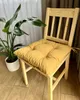A yellow seat cushion is placed on a wooden chair next to a potted plant. Produktbild-Vorschau