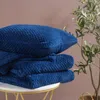 A stack of blue blankets and a pillow on a white table, with a plant in the background. Podgląd zdjęcia produktu