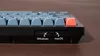 A close-up side view of a black mechanical keyboard with blue and red keycaps. The image highlights the USB-C port and two switches labeled 'Windows' and 'macOS'. Náhľad obrázku produktu