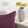 A close-up of a purple cushion with a red tag, next to a vase with yellow flowers. Produktbild-Vorschau
