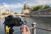 A hand inserts an SD card into a camera with a blurred cityscape in the background. Produktbild-Vorschau
