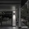 An outdoor wall light illuminates a modern house exterior at dusk. Produktbild-Vorschau