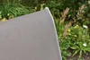 Close-up of the edge of a taupe fabric chair seat with a silver frame, with a garden in the background. Produktbild-Vorschau