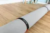 A rolled-up rug with black and red straps on a wooden floor. Produktbild-Vorschau