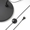A close-up view of the base and power cord of a black floor lamp. Produktbild-Vorschau