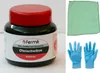 A product shot of a jar of Fermit Ofenschwärze, a cleaning product for ovens, grills, and fireplaces, along with a green cloth and a pair of blue gloves. Produktbild-Vorschau