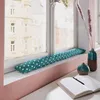 A teal and white polka dot draft stopper lies on a windowsill, with two decorative vases and an open notebook on the desk in the foreground. Produktbild-Vorschau