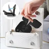 A hand is placing a black wireless charger into a white textured handbag. Produktbild-Vorschau