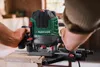 A person is using a green and black Parkside router on a wooden surface in a workshop. Produktbild-Vorschau