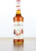 A bottle of Monin Caramel syrup is displayed upright on a wooden surface against a white background. Produktbild-Vorschau