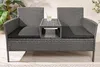 A gray rattan garden bench with a built-in table and black cushions, set on a wooden deck with some greenery in the background. Produktbild-Vorschau