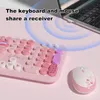A pink keyboard and mouse set are shown on a pink surface, with a laptop in the background. Blue concentric circles emanate from the laptop, suggesting a wireless connection. Produktbild-Vorschau