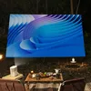 An outdoor movie night setup with a projector displaying an abstract image on a screen, a small table with snacks and drinks, and chairs. Produktbild-Vorschau