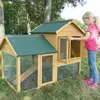 A young girl is interacting with a wooden rabbit hutch in an outdoor setting with trees and grass. Produktbild-Vorschau