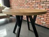 A round wooden table with black legs is placed in front of a brick wall and a light-colored sofa. Náhled obrázku produktu